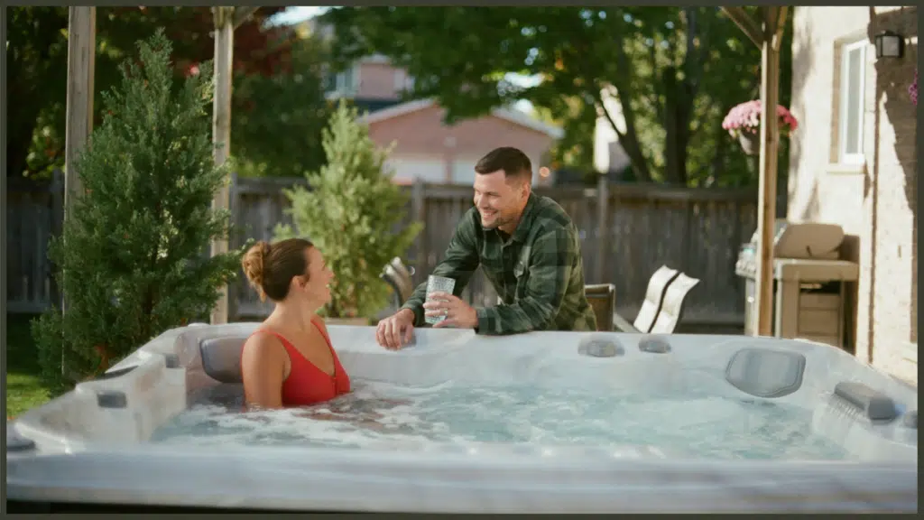 A calm, peaceful view of an adult relaxing deeply in a bubbling hot tub at dusk, resting their arms comfortably on the smooth acrylic rim with their head elevated well above the water line.