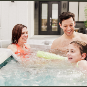 A professional technician in corporate workwear using specialized diagnostic tools to check the internal plumbing, high-performance pump connections, and control pack of an open luxury swim spa cabinet.