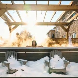 A side-angle view of a premium Hydropool swim spa operating in a modern garden at dusk, showcasing its heavy-duty insulated thermal cover half-retracted to reveal warm, steaming water under elegant LED lighting.
