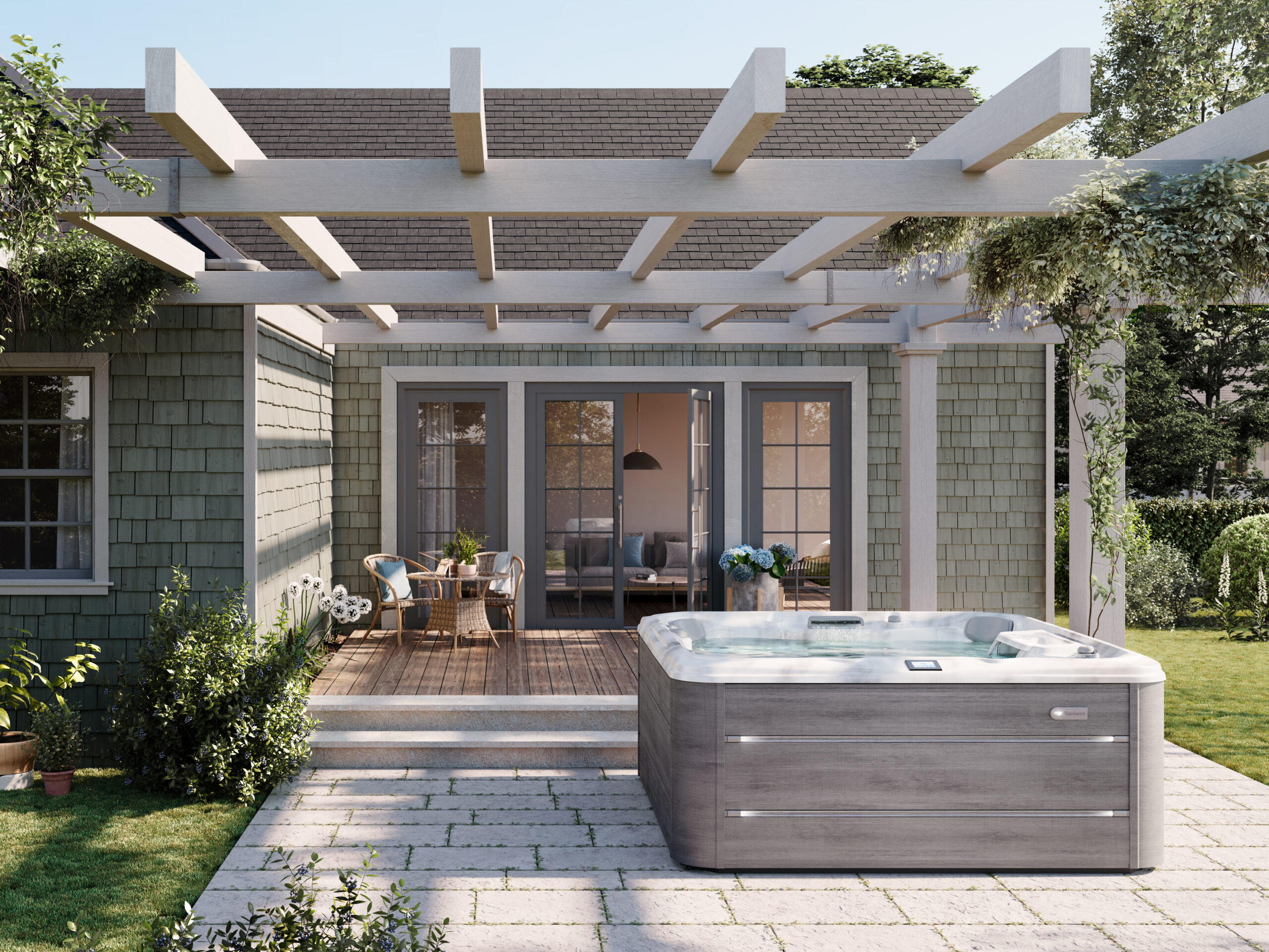 Wide lifestyle photograph of a family enjoying a Sundance 780 Series Chelsee hot tub with a Platinum acrylic shell and Vintage Oak cabinetry, beautifully integrated alongside an outdoor dining table in a luxury garden setting.
