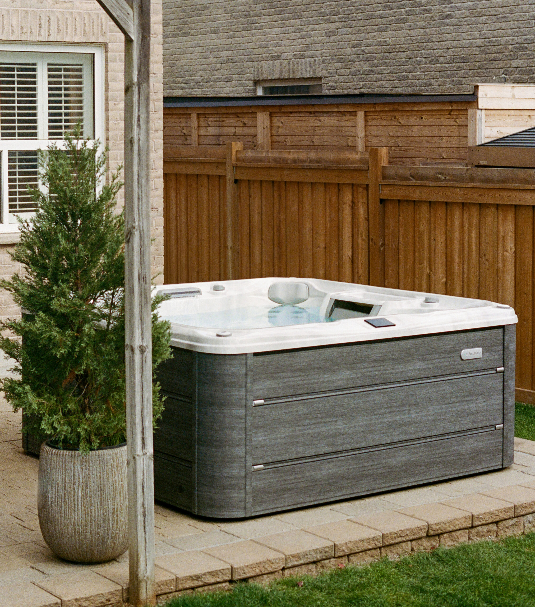 Lifestyle photograph of a couple relaxing together in a Sundance 780 Series Chelsee hot tub featuring a Platinum acrylic shell and Vintage Oak cabinetry, set within a luxury evening garden design.
