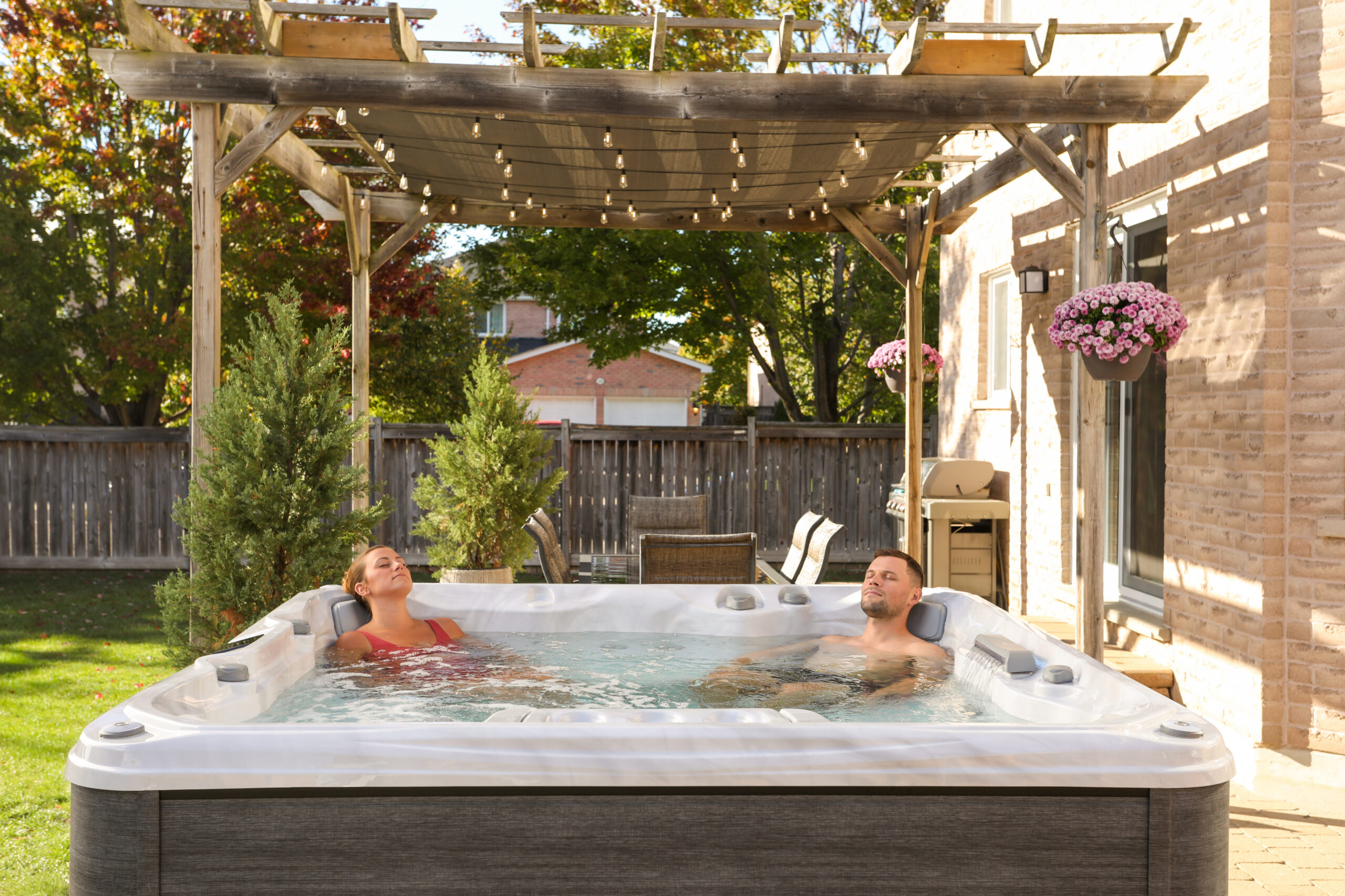 Lifestyle photograph of a couple relaxing together in a Sundance 780 Series Chelsee hot tub featuring a Platinum acrylic shell and Vintage Oak cabinetry, set within a luxury evening garden design.