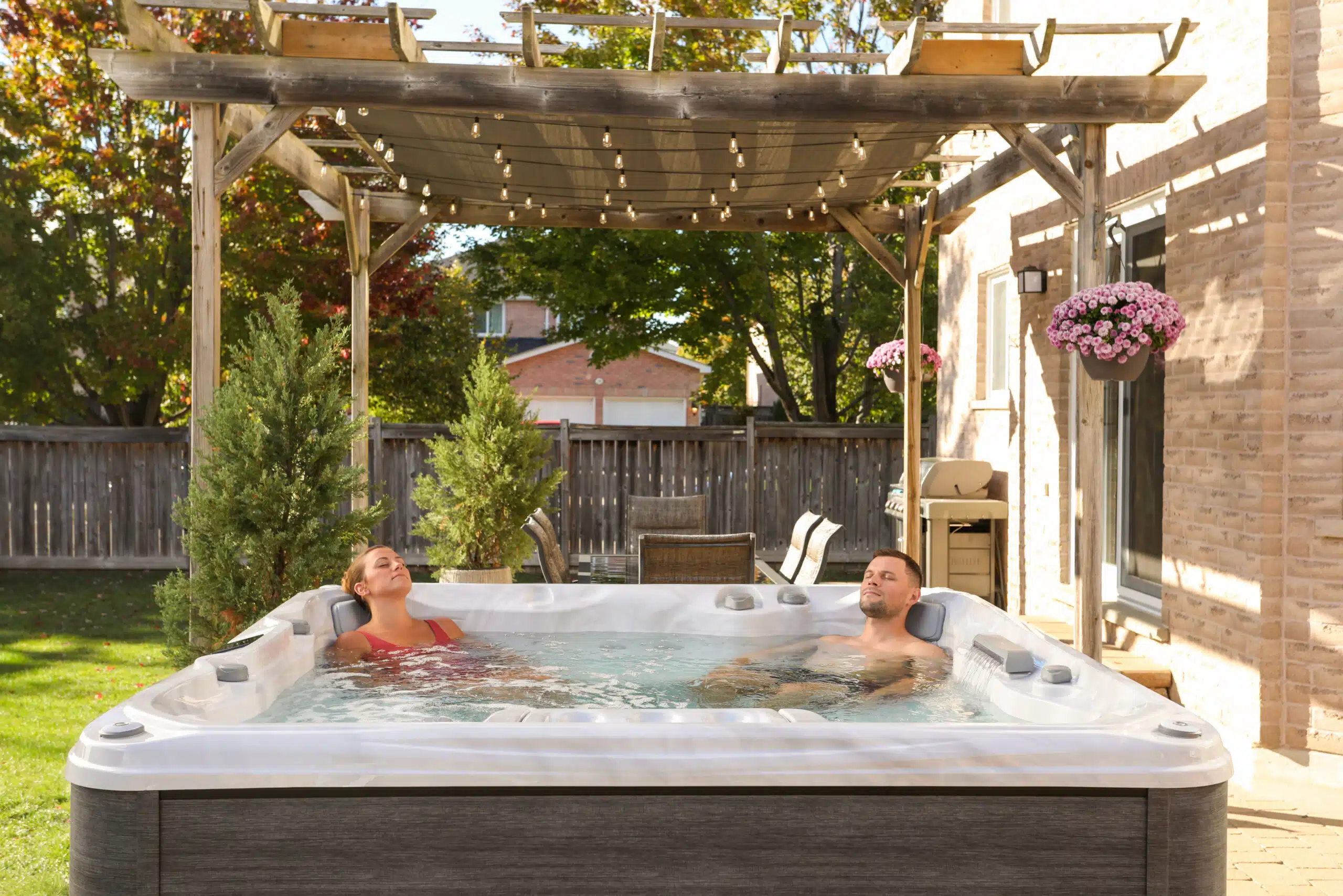 Lifestyle photograph of a couple relaxing together in a Sundance 780 Series Chelsee hot tub featuring a Platinum acrylic shell and Vintage Oak cabinetry, set within a luxury evening garden design.