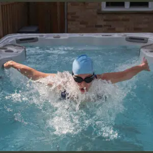A side view of an elegant, hard-shell swim spa installed above-ground on a timber deck, featuring crisp LED underwater lighting and a powerful jet stream creating a smooth current at the front of the lane.