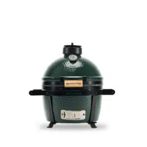A professional e-commerce product shot of the Big Green Egg MiniMax Portable BBQ, showcasing the iconic dimpled green ceramic kamado nestled securely inside its heavy-duty black steel transportation carrier with dual easy-to-grip handles.