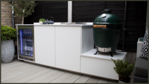 A custom-built luxury outdoor kitchen island featuring an integrated Big Green Egg ceramic kamado charcoal grill alongside premium stainless steel storage drawers and sleek black granite worktops.