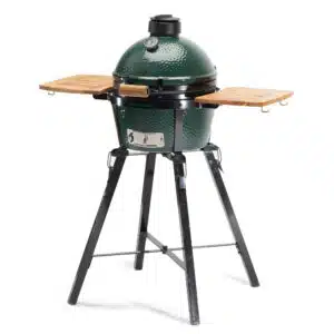 A professional e-commerce product shot of the Big Green Egg Foldable MiniMax Stand with Acacia Shelves, showcasing the compact black steel folding frame and two slatted premium acacia wood side tables attached to the sides.
