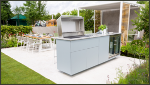 A stunning contemporary kitchen extension featuring massive floor-to-ceiling bi-fold glass doors fully opened to seamlessly connect a luxury indoor dining space with a modern flush-level outdoor garden patio.