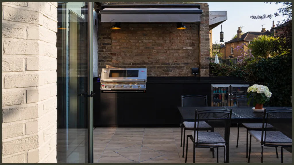 A clever compact garden project in Hornsey, Enfield, featuring a sleek bespoke outdoor kitchen with a Beefeater grill and a retractable Pratic fabric awning over a modern dining area.