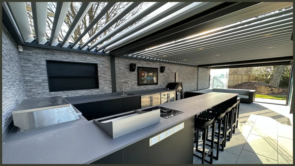 A luxury completed backyard project in Brentwood, Essex, showcasing a premium built-in outdoor kitchen with stone worktops and a contemporary black aluminium louvred pergola over a modern dining area.