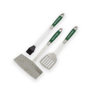 A professional e-commerce product shot of the Big Green Egg Stainless Steel BBQ Tool Set, displaying the heavy-duty spatulas, comfort-grip handles, and a high-quality basting brush laid out neatly.