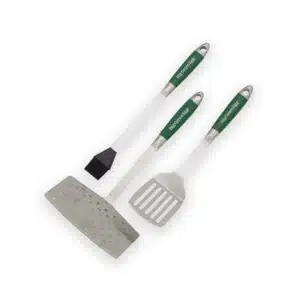 A professional e-commerce product shot of the Big Green Egg Stainless Steel BBQ Tool Set, displaying the heavy-duty spatulas, comfort-grip handles, and a high-quality basting brush laid out neatly.